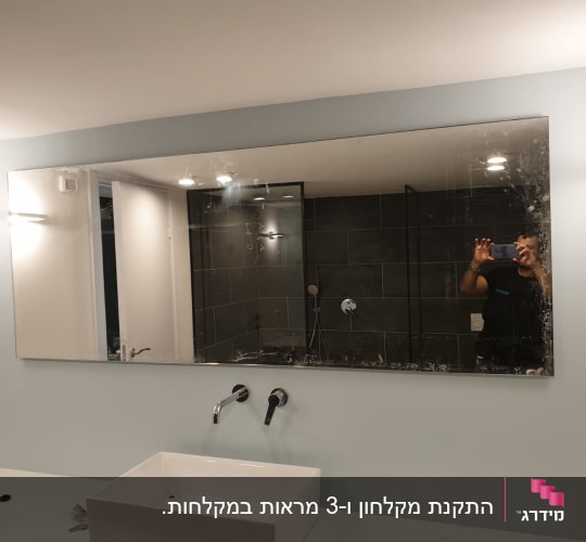 מראה גדולה מעל כיור בחדר רחצה המשקפת מקלחון